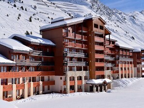 Um hotel com várias andares e varandas, com uma paisagem de montanha nevada ao fundo.