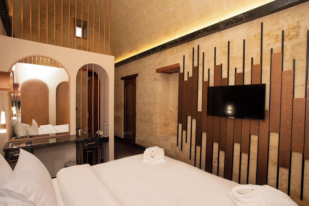 A hotel room with a large bed, a TV mounted on the wall, a mirror, and a wooden panel design.