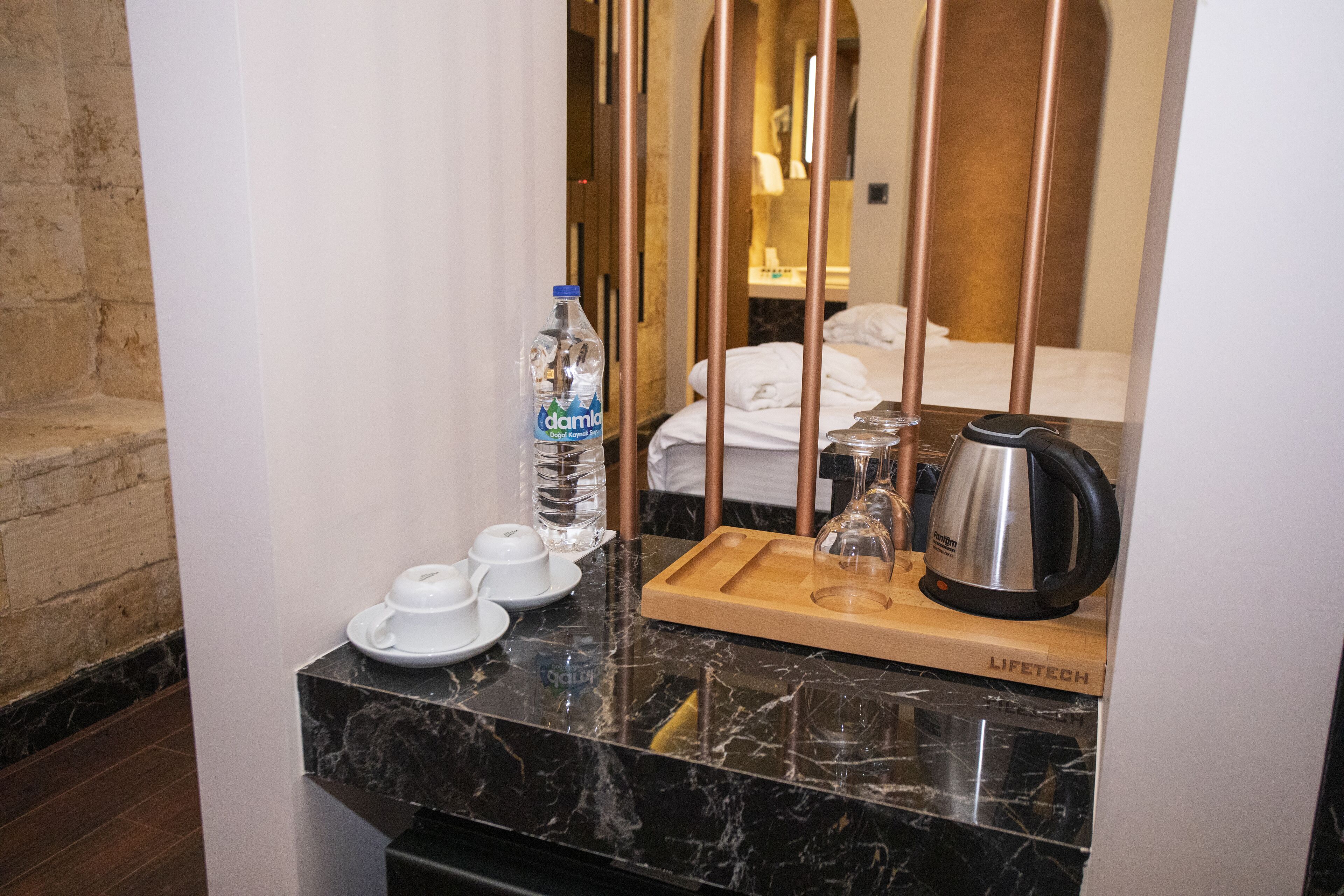 Quarto de hotel com bancada de mármore, garrafa de água, xícaras de chá, bandeja e chaleira.