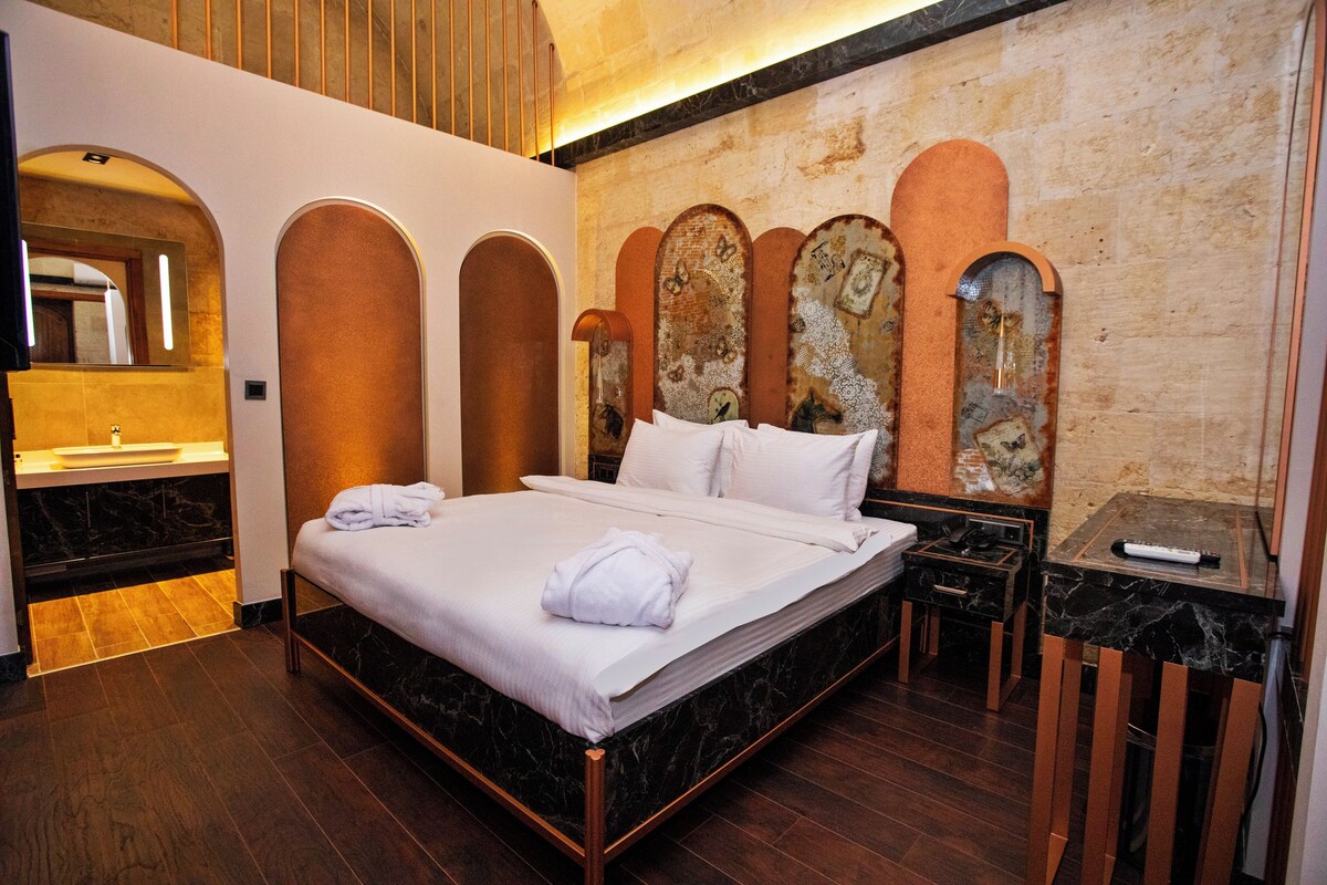 Ein Hotelzimmer mit einem großen Bett, Holzboden, einem Badezimmer mit Marmorfliesen und einem außergewöhnlichen Wanddesign mit Bogen.