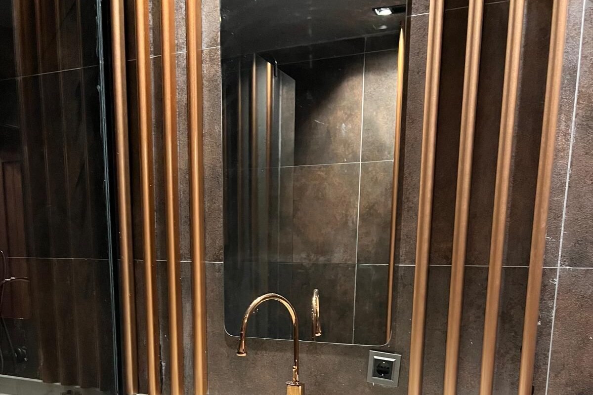 A modern bathroom with a large marble sink, a gold faucet, and a mirror with vertical wooden panels.