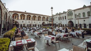 An outdoor dining area with tables and chairs, surrounded by a building with arched windows and a tiled roof. - Bayazhan Butik Hotel (Gaziantep)