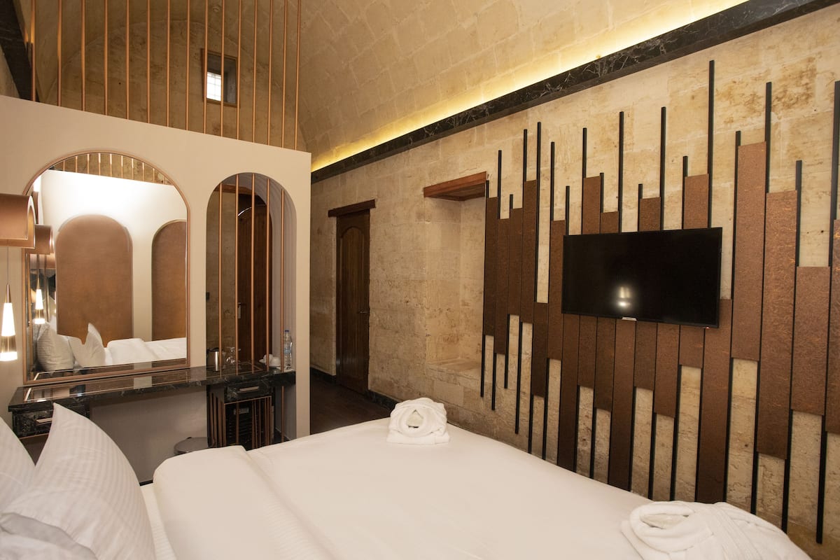 Ein Hotelzimmer mit einem großen Bett, einem flachbildfernseher an der Wand, einem Spiegel und einer Wandverkleidung aus Holz.