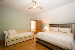 A bedroom with a bed, a sofa, a ceiling fan, and a door leading to another room.