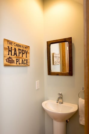 Ein Badezimmer mit einem Holzschild mit der Aufschrift 'The cabin is my happy place' und einem Spiegel mit Holzrahmen.