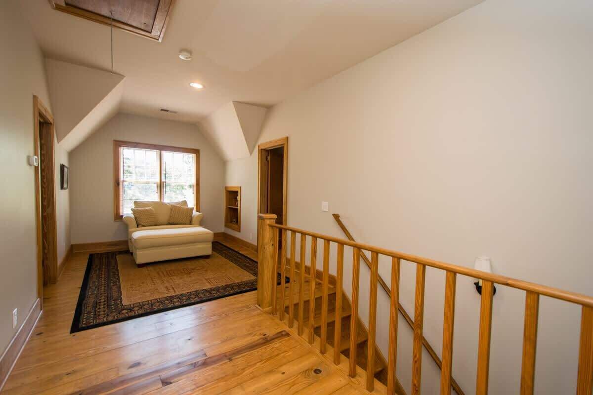 Una habitación amplia con una escalera de madera, un sofá y un ventanal grande.