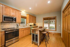 A kitchen with wooden cabinets, a stainless steel oven, a microwave, a coffee maker, and a bar stool.