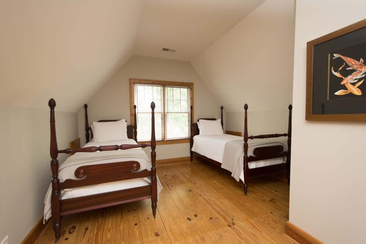 A bedroom with two wooden four-poster beds, a large window, and a framed picture on the wall.