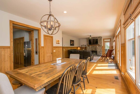 A spacious dining area with a wooden table and chairs, a stone fireplace, and large windows allowing natural light. - Lakefront 3BR w/ Private Dock + Firepit | Free Tix (Mill Spring)