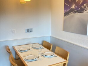 A dining area with a table set for four, light blue chairs, a wall-mounted light fixture, and a painting of a mountain landscape.