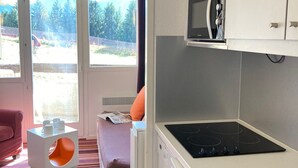 Cocina compacta con estufa, microondas y ventana con vistas a árboles y una valla.