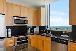 A modern kitchen with wooden cabinets, a stainless steel microwave, and a dishwasher. - Sapphire #1501 | Luxury Beachfront Resort • 15th Floor Panoramic Gulf Views • Pool (South Padre Island)