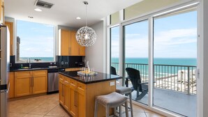 Una cocina moderna con una isla grande, armarios de madera y vista al océano a través de amplios ventanales corredizos.