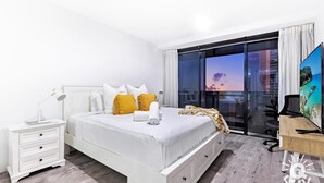 A modern hotel room with a large bed, a desk, a chair, and a TV.