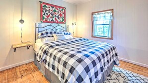 A bedroom with a bed, a quilt, a nightstand, a wall-mounted quilt, a window with a curtain, and a wooden floor. - 'Lochview Lodge' Idyllic Farmhouse in Grove! (Grove)