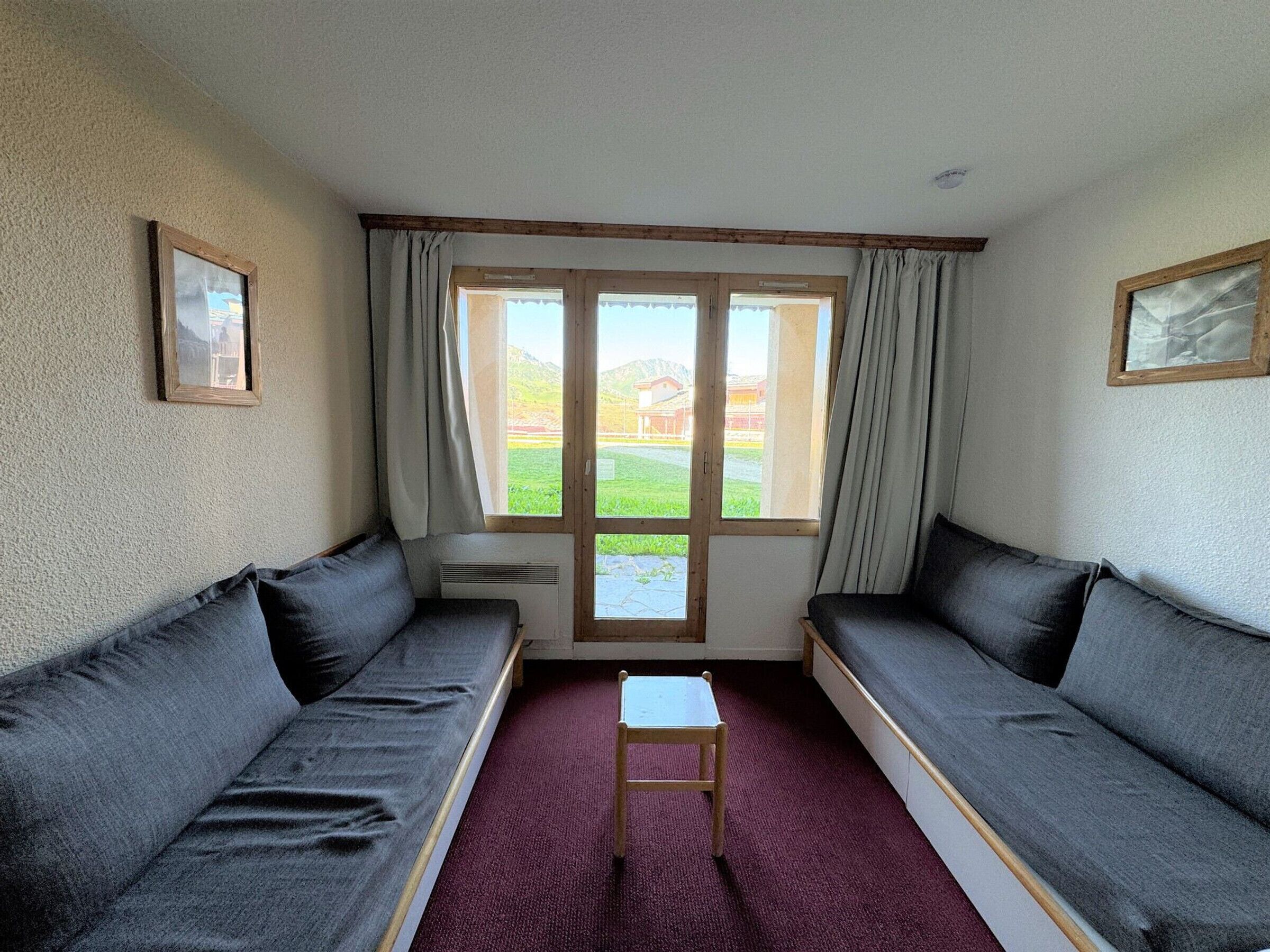 A room with two dark grey sofas, a small wooden table, and a window with curtains.