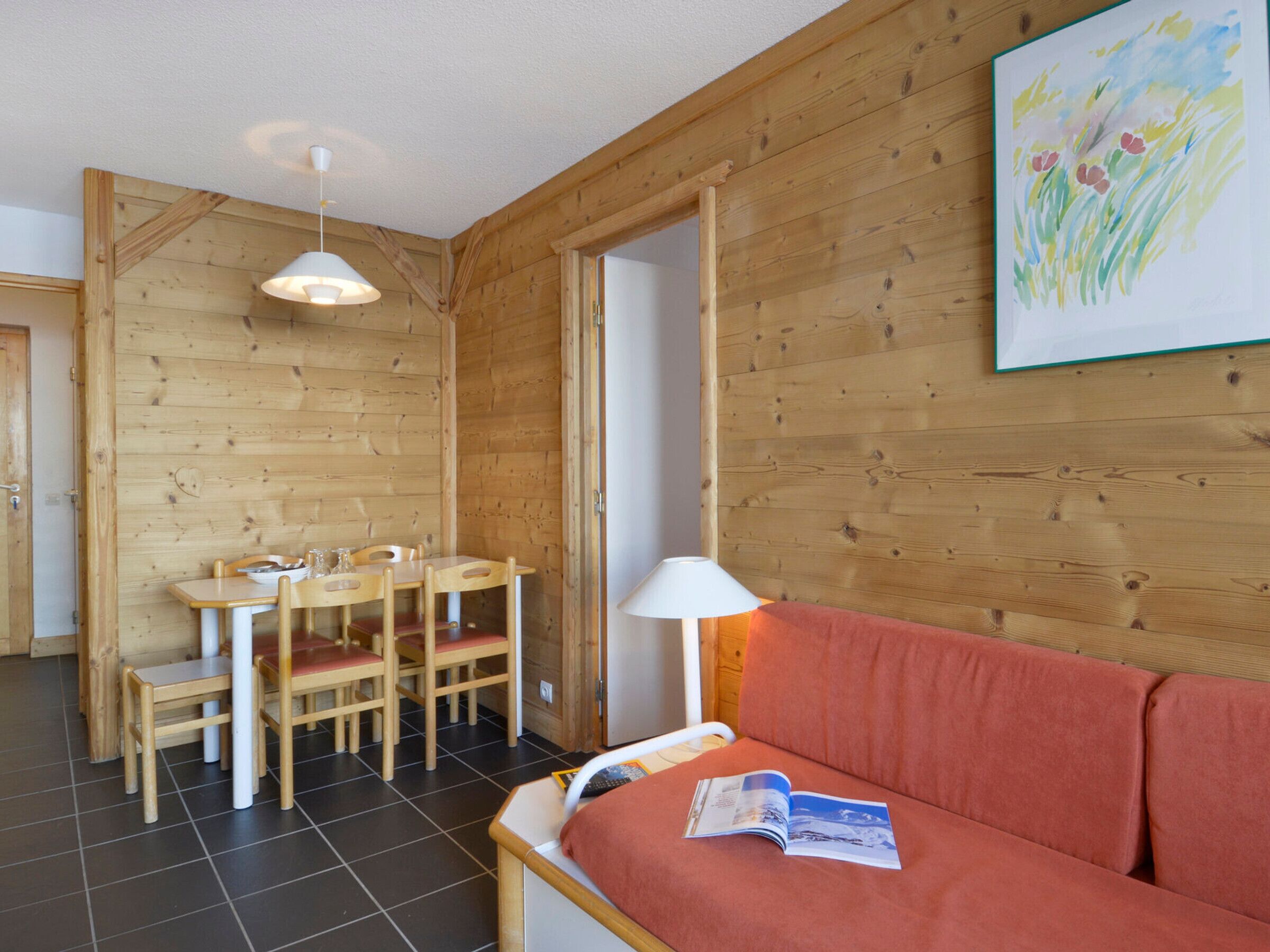 Ein gemütliches Zimmer mit Holzeinrichtung, einem Esstisch mit Stühlen, einer Couch und einer Lampe.