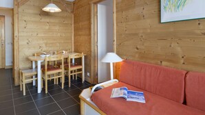A cozy room with a wooden interior, a dining table with chairs, a sofa, and a lamp.
