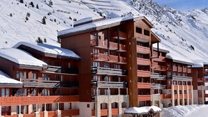 A multi-story hotel with balconies, set against a snowy mountain backdrop.