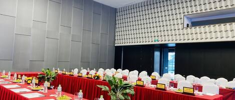 A conference room with red tables, white chairs, nameplates, water bottles, and potted plants.