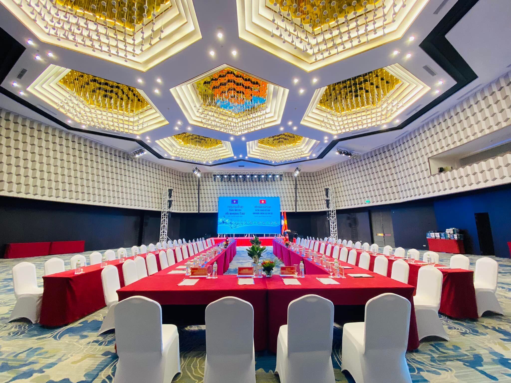 A conference room with a long table, white chairs, and a stage with a screen.