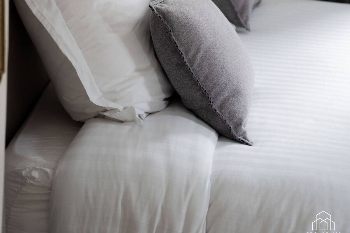 A neatly made bed with white and gray pillows, a modern wall-mounted light fixture, and a minimalist design.