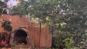 Un arco de piedra que da acceso a un jardín con cerca de bambú, rodeado de diversas plantas y árboles.