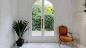 Una habitación con una puerta blanca que da a un jardín, una planta en maceta y un sillón tapizado en rojo.