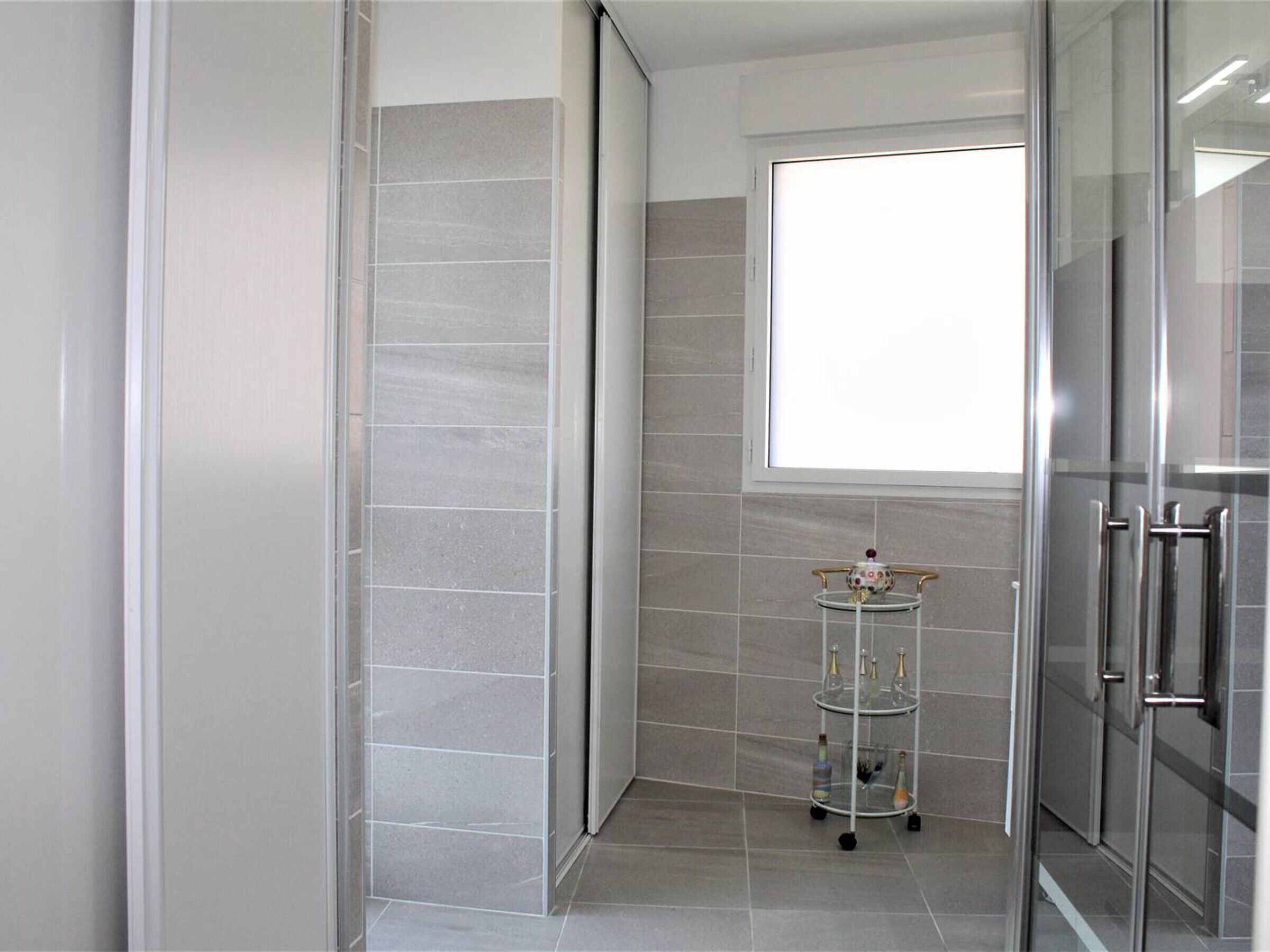 Een moderne badkamer met een douchecabine van glas, een klein plankje met flessen en een raam voor natuurlijk licht.