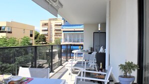 A balcony with white furniture, a potted plant, and a view of other buildings. - New 3-Room Apartment with Terrace and Garage, Cagnes-sur-Mer (Cagnes-sur-Mer)