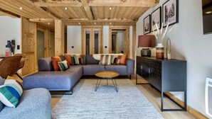 Una sala de estar acogedora con techo de madera, un sofá modular, una mesita redonda y un aparador con objetos decorativos.
