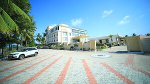 A hotel entrance with a paved driveway, palm trees, and a white car parked. - Royal Rich County (Gangavathi)