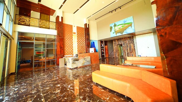 A spacious lobby with a marble floor, a reception desk, and a large digital screen displaying a fish. - Royal Rich County (Gangavathi)