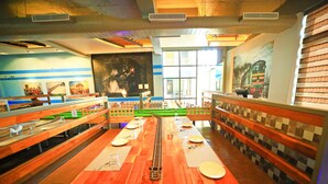 A restaurant with wooden benches and tables, a model train track, and various paintings on the walls. - Royal Rich County (Gangavathi)