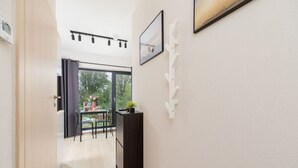 A hallway with a wooden floor, a black desk with a plant, and a dining area with a table and chairs. - Stylish Studio in Krakow | Air Conditioning | Close to the Station (Kraków)