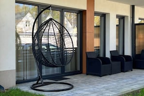A modern outdoor seating area with a unique spherical chair, large windows, and a clean, contemporary building facade. - Cozy Apartment | Terrace, Sauna and Gym (Międzywodzie)