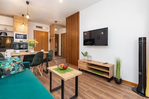 A modern living room with a sofa, a coffee table, a TV, and a kitchen area in the background.