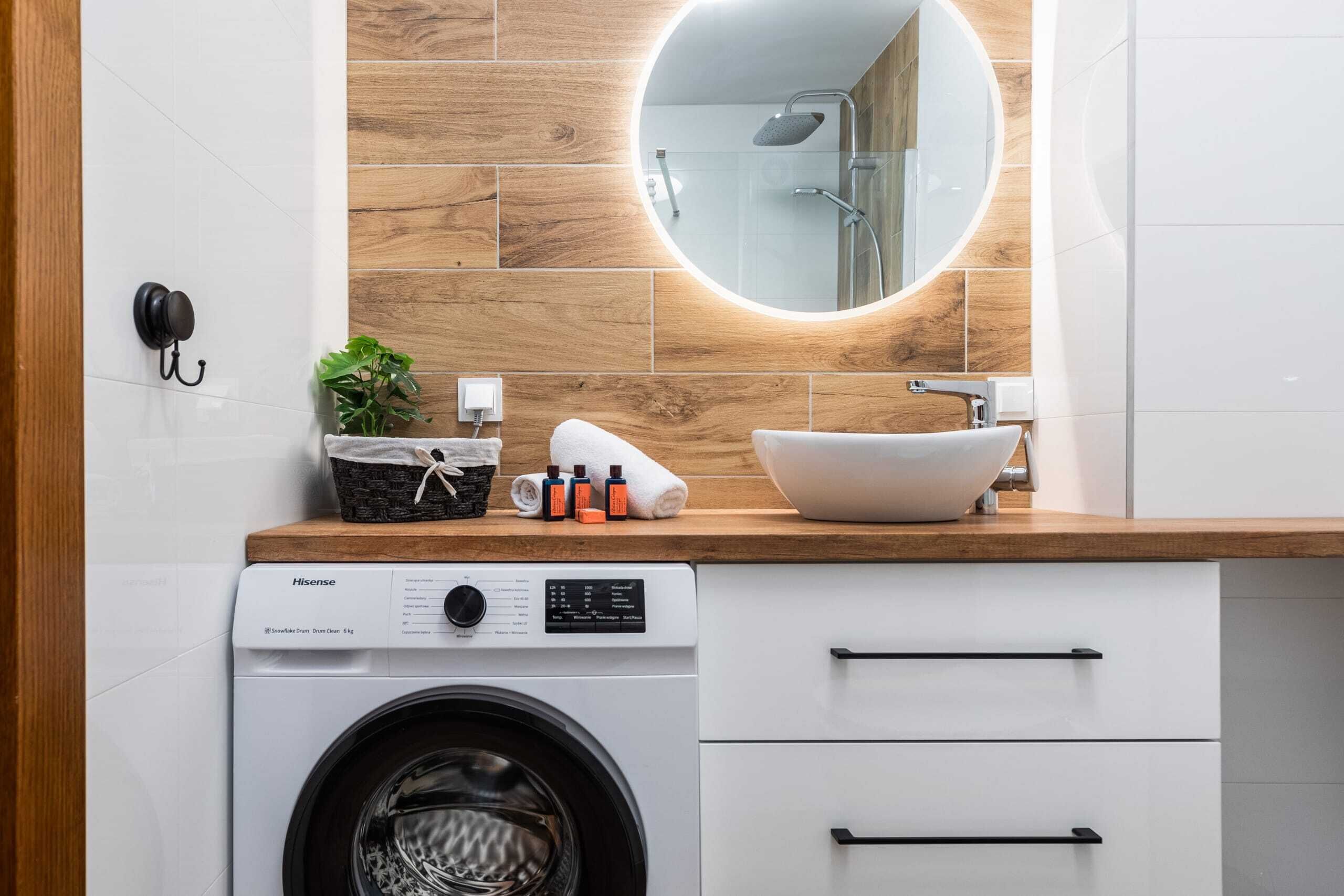 A modern bathroom with a wooden wall, a round mirror, a sink, and a washing machine.