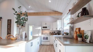 A modern kitchen with white cabinetry, a central island, and wooden beams on the ceiling. - A Wave from it All, close to Lake Huron & Bayfield (Bayfield)
