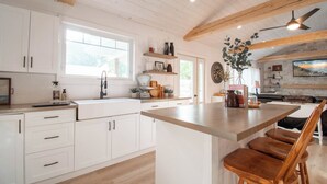 A modern kitchen with white cabinets, a large island with bar stools, a window, and a ceiling fan. - A Wave from it All, close to Lake Huron & Bayfield (Bayfield)