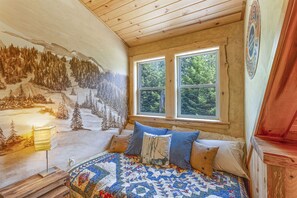 Cozy bedroom with a large bed, wooden ceiling beams, and a scenic wall mural.