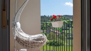 Una silla colgante blanca en un balcón con vistas a un paisaje verde y una maceta roja.