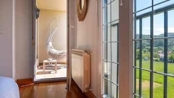 Een kamer met uitzicht op een groen landschap door grote ramen, een witte radiator en een hangstoel.
