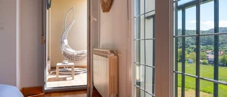 Una habitación con vistas a un paisaje verde a través de amplios ventanales, un radiador blanco y un sillón colgante.