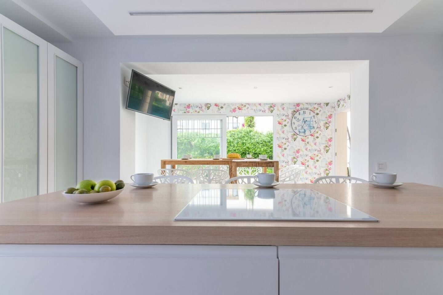 Une cuisine moderne avec un plan de travail en bois, un saladier rempli de fruits et un coin repas comprenant une table et des chaises.