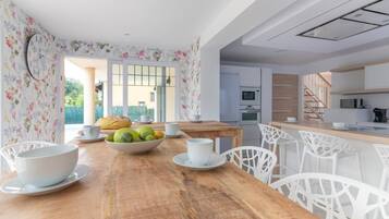 A dining area with a wooden table set for breakfast, white chairs, and a bowl of fruit.