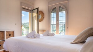 Un letto rifatto con lenzuola e asciugamani bianchi, una testiera in legno e vista attraverso un'ampia finestra ad arco.