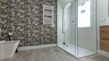 Un bagno con doccia, una vasca da bagno bianca e un rivestimento a motivi.