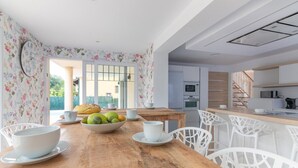 Una cucina moderna con mobili bianchi, un tavolo da pranzo in legno e sedie bianche. Sul tavolo c'è una ciotola di frutta e un orologio al muro.
