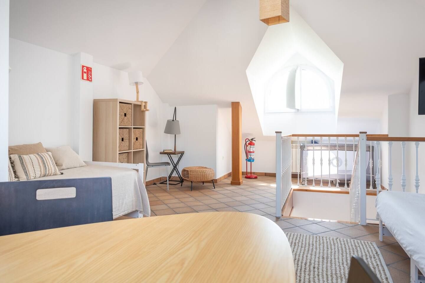 Een slaapkamer met een hoogslaper, een bureau, een stoel, een lamp, een boekenplank en een brandblusser.